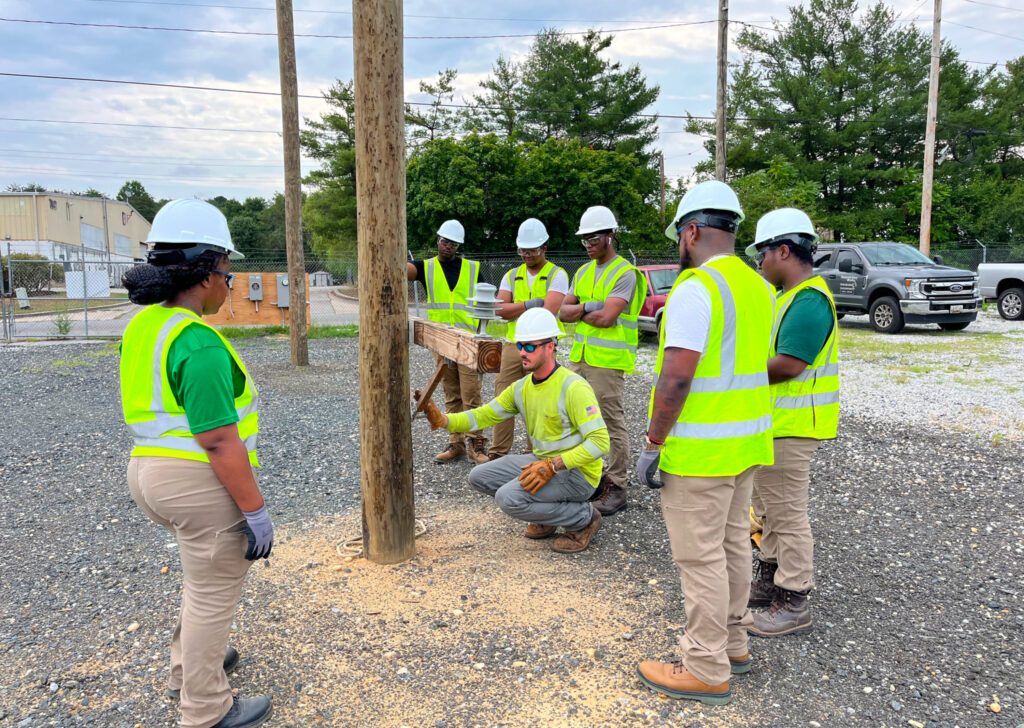 trainees in safety gear standing around an instructor working on a power line pole