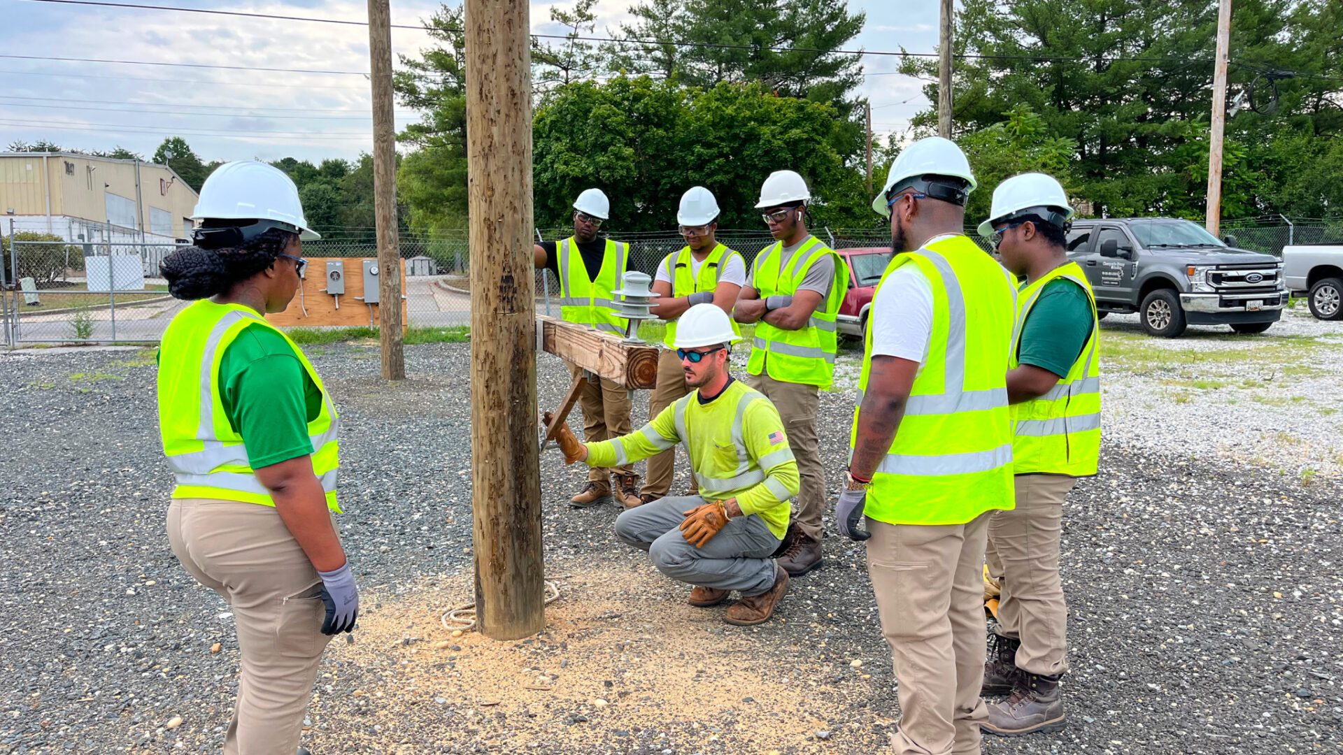 trainees in safety gear standing around an instructor working on a power line pole