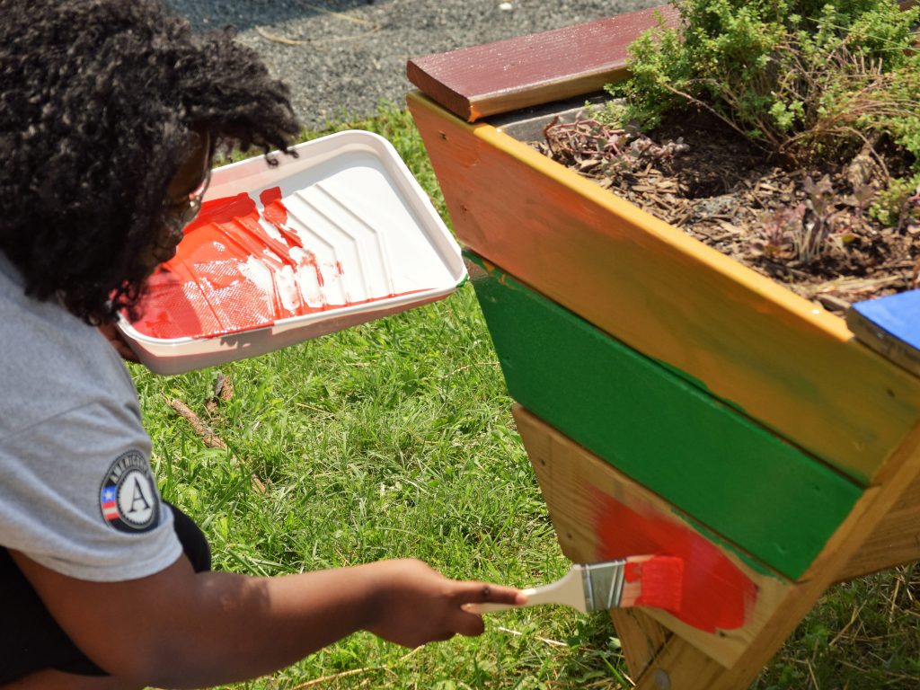 a volunteer painting a raised garden bed box